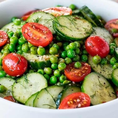 Close-up view of Dill Pea and Cucumber Salad in a white bowl garnished with halved cherry tomatoes.