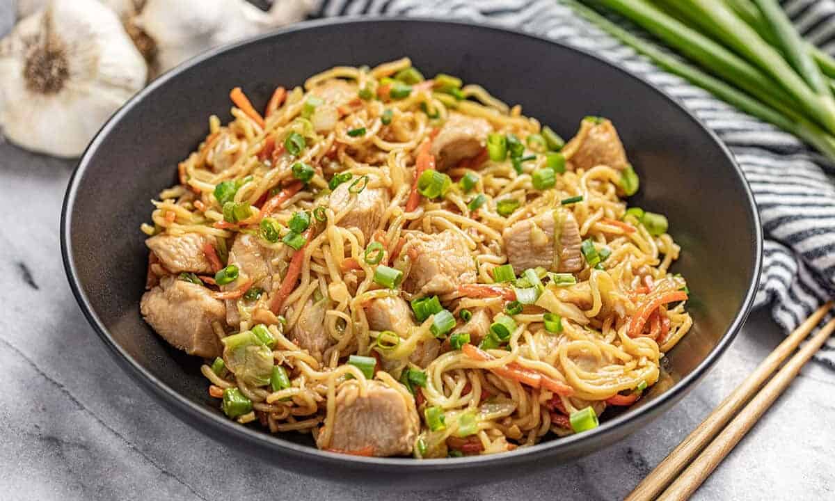 Angled view of Chicken Chow Mein in a black bowl with chopsticks.