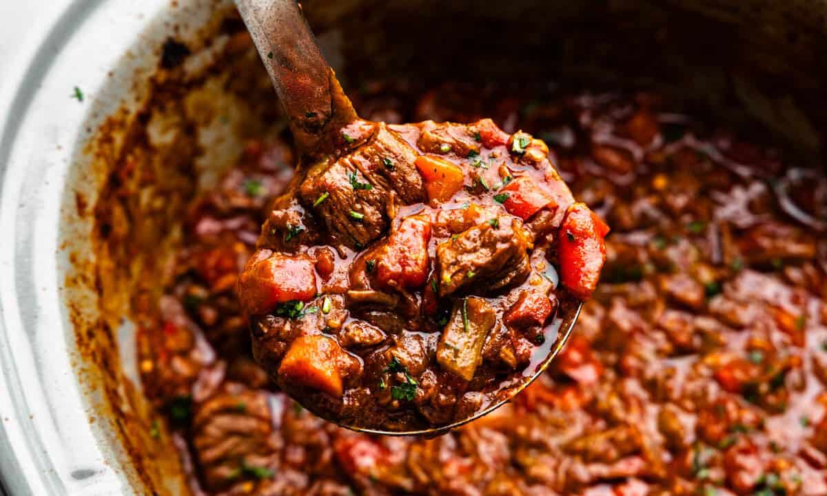 A ladle scooping out a helping of Texas beef chili from the slow cooker.