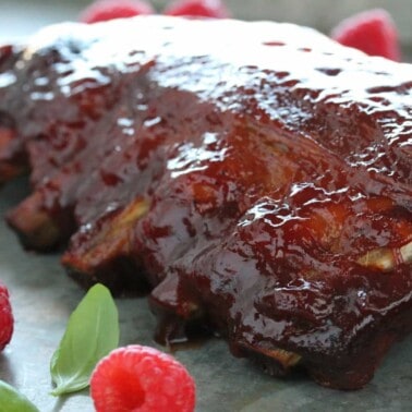 Baby back ribs smothered in raspberry chipotle bbq sauce, surrounded by fresh raspberries