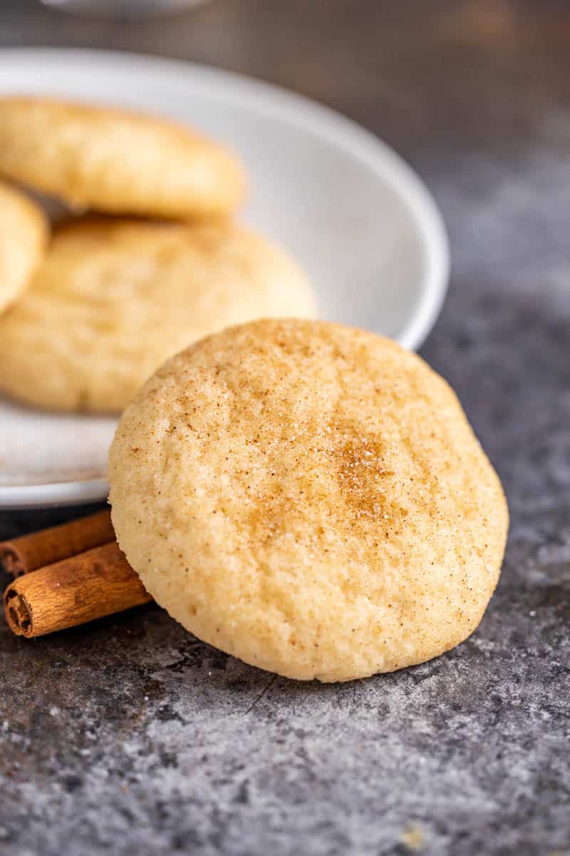 A snickerdoodle cookie leaning against a white platter with more cookies.