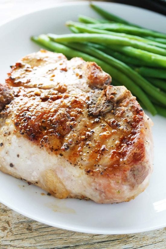 Close-up of a think cut, juicy bone-in grilled pork chop on a plate with green beans