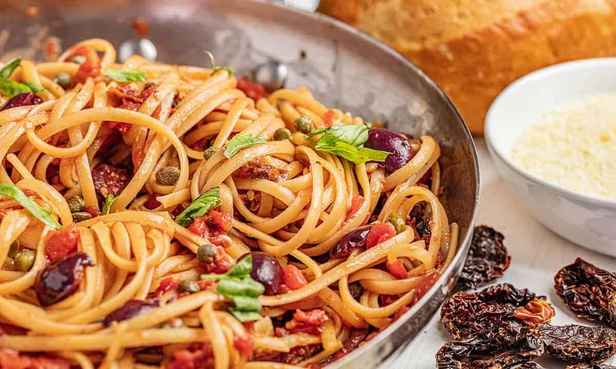 Pasta puttanesca with fresh basil in a skillet.